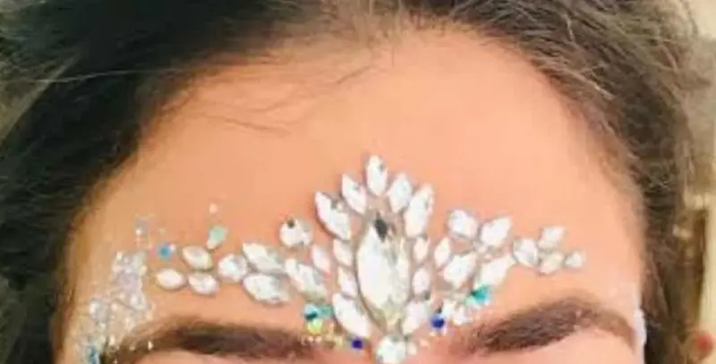 Crown of face gems and glitter painted across an adult guest's forehead