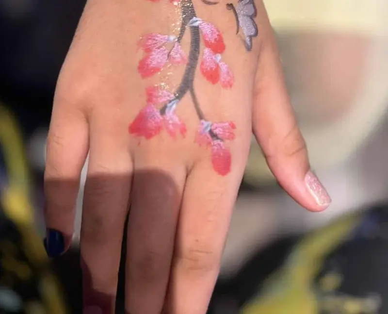 Pink cherry blossom face paint design painted on a child's hand and wrist
